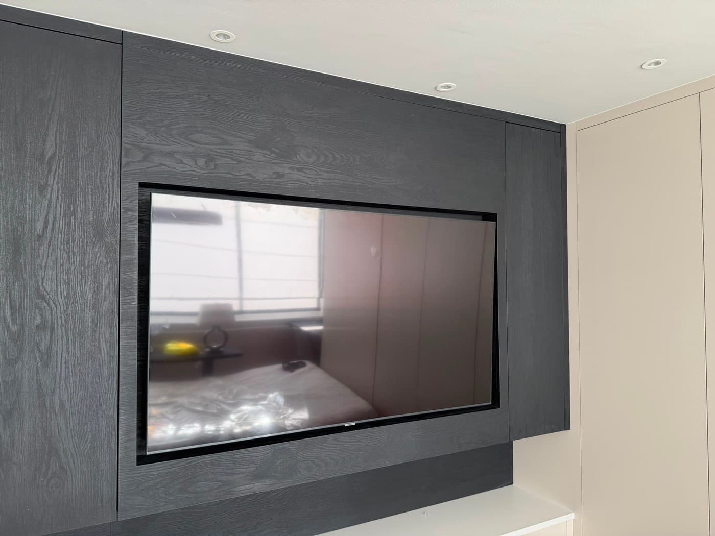 Media wall with a television set into dark oak panelling, lit by recessed ceiling lights